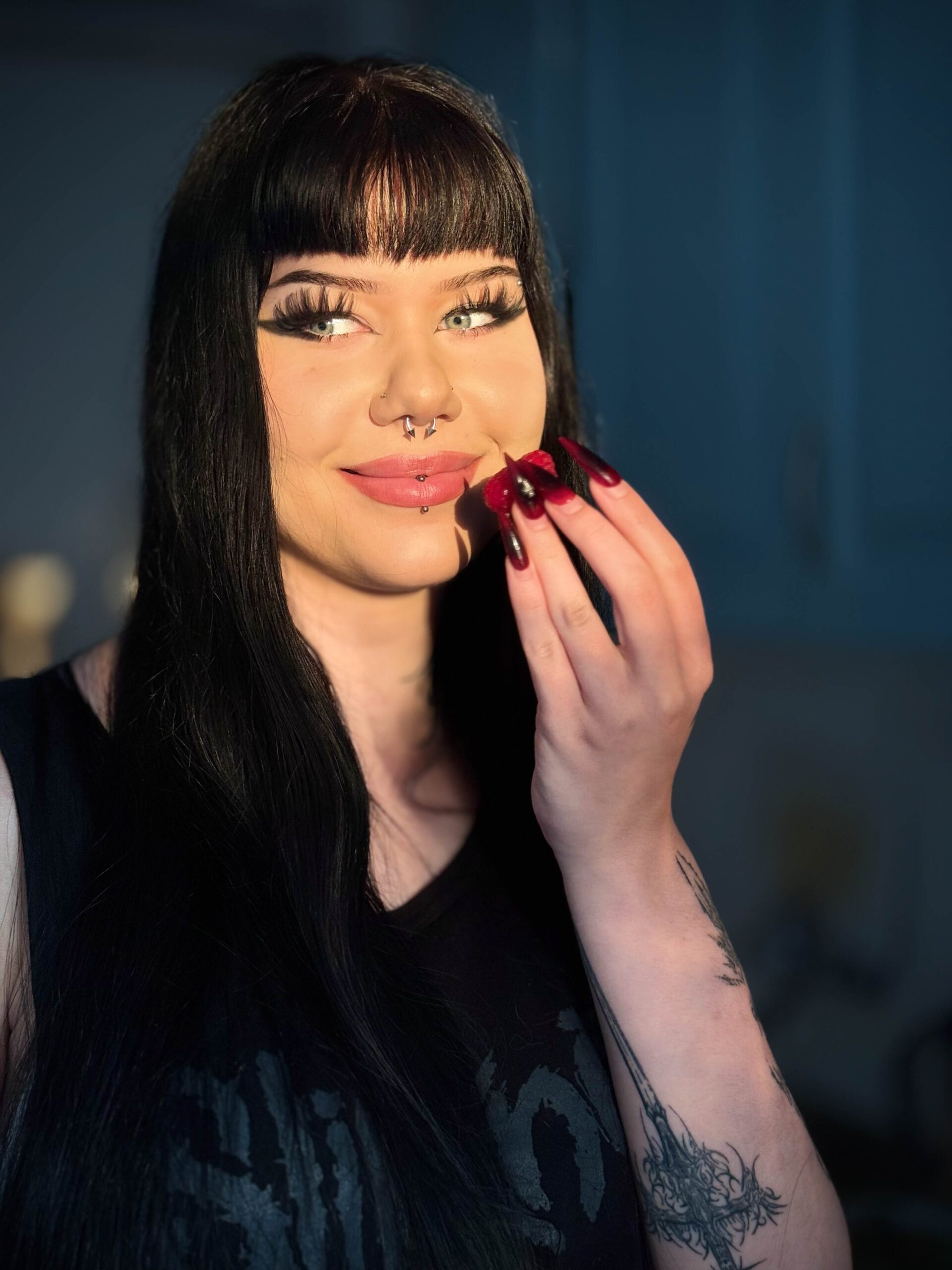 13. Młoda brunetka o mocnym gotyckim makijażu je truskawkę w promieniach zachodzącego słońca