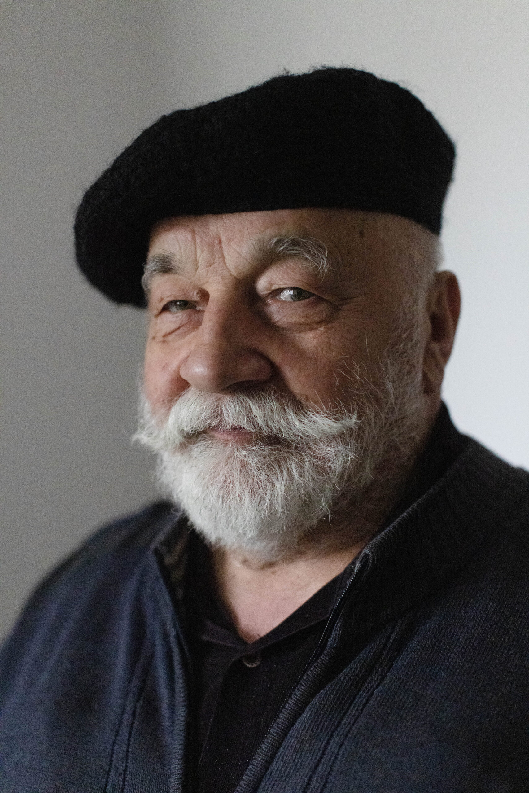 Starszy pan z siwą brodą i wąsem, w czarnym berecie z półuśmiechem pozuje do zdjęcia