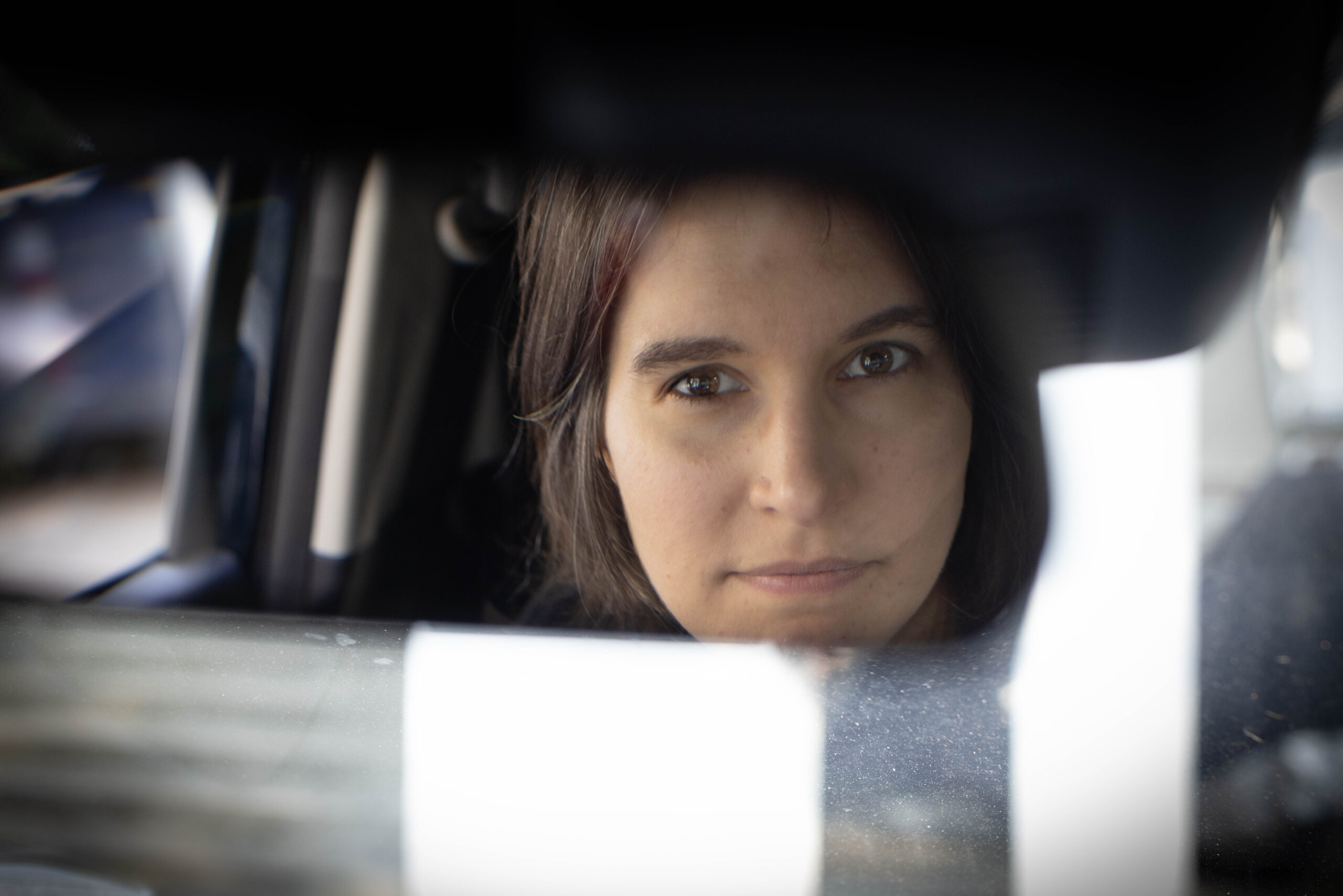 Młoda brunetka odbija się w lusterku samochodowym pozując do zdjęcia, skupiony wzrok