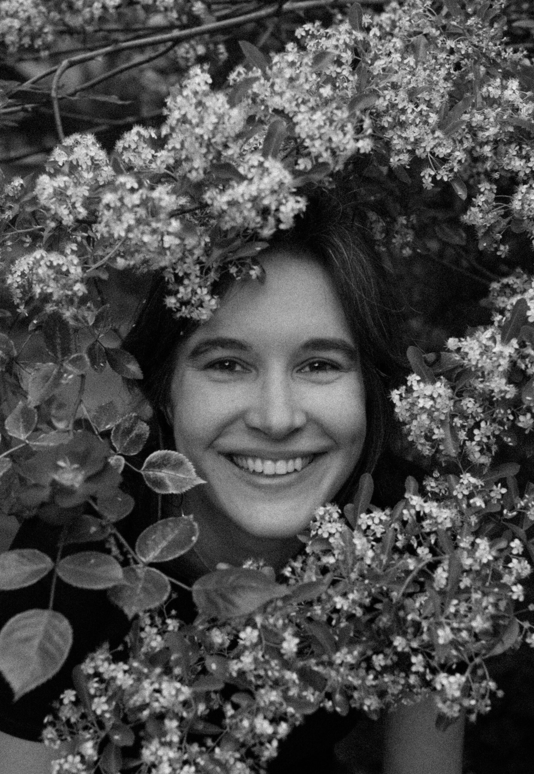 Czarno-biały portret młodej uśmiechniętej brunetki pozującej wśród kwitnących gałęzi