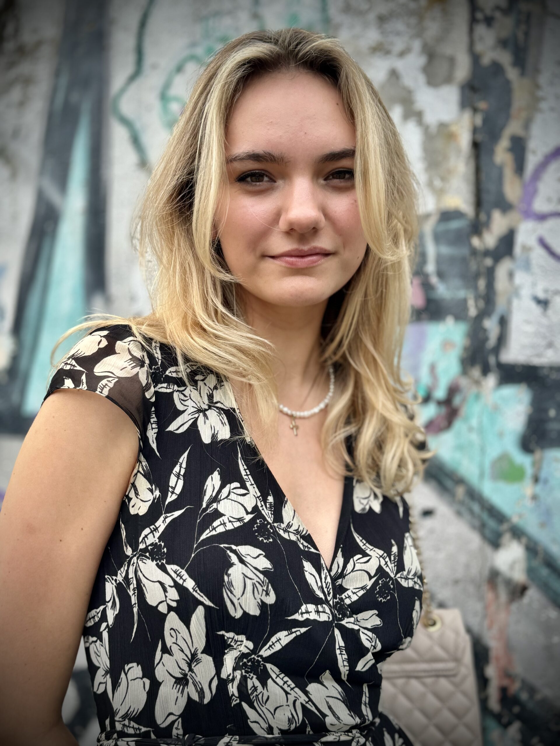 młoda piękna dziewczyna blondynka patrzy wprost w obiektyw, w sukience w czarno-białe kwiaty i perłowym naszyjniku