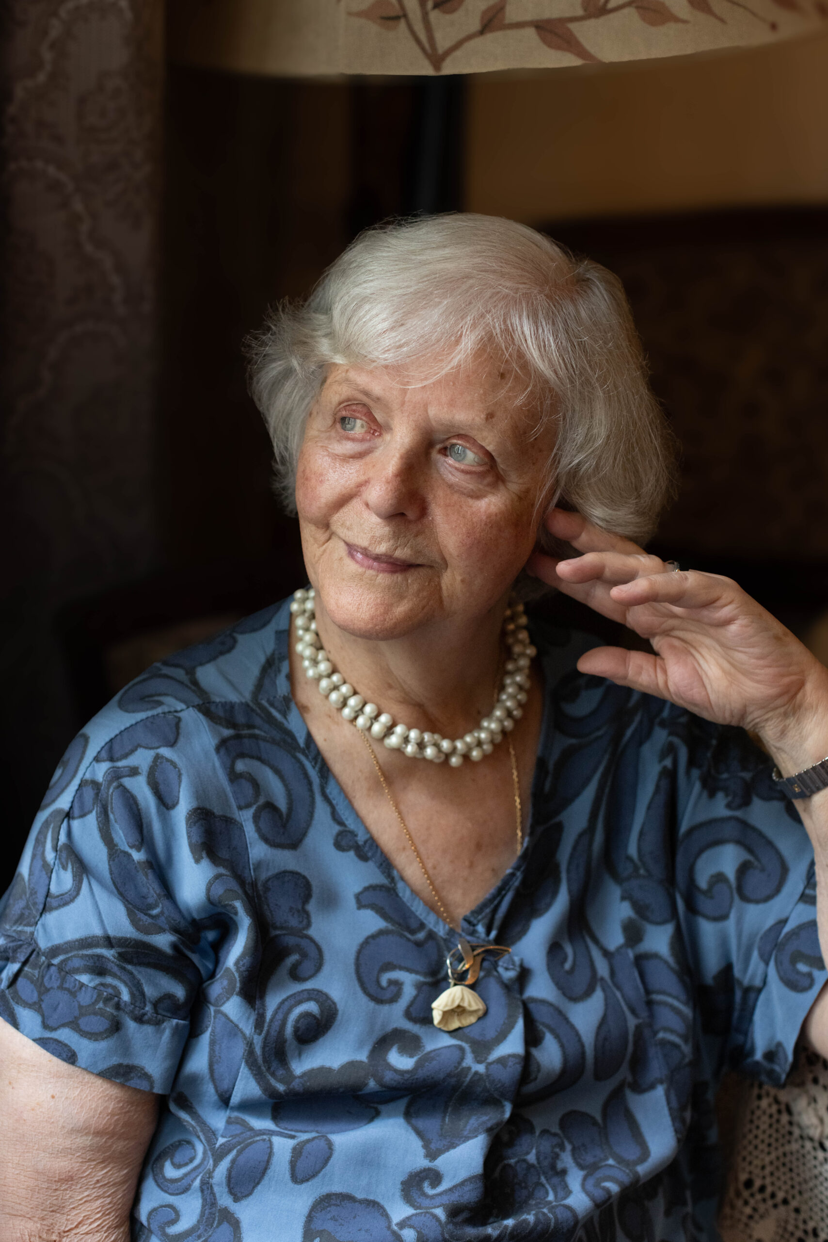 starsza siwa kobieta z uśmiechem siedzi w fotelu i patrzy w okno