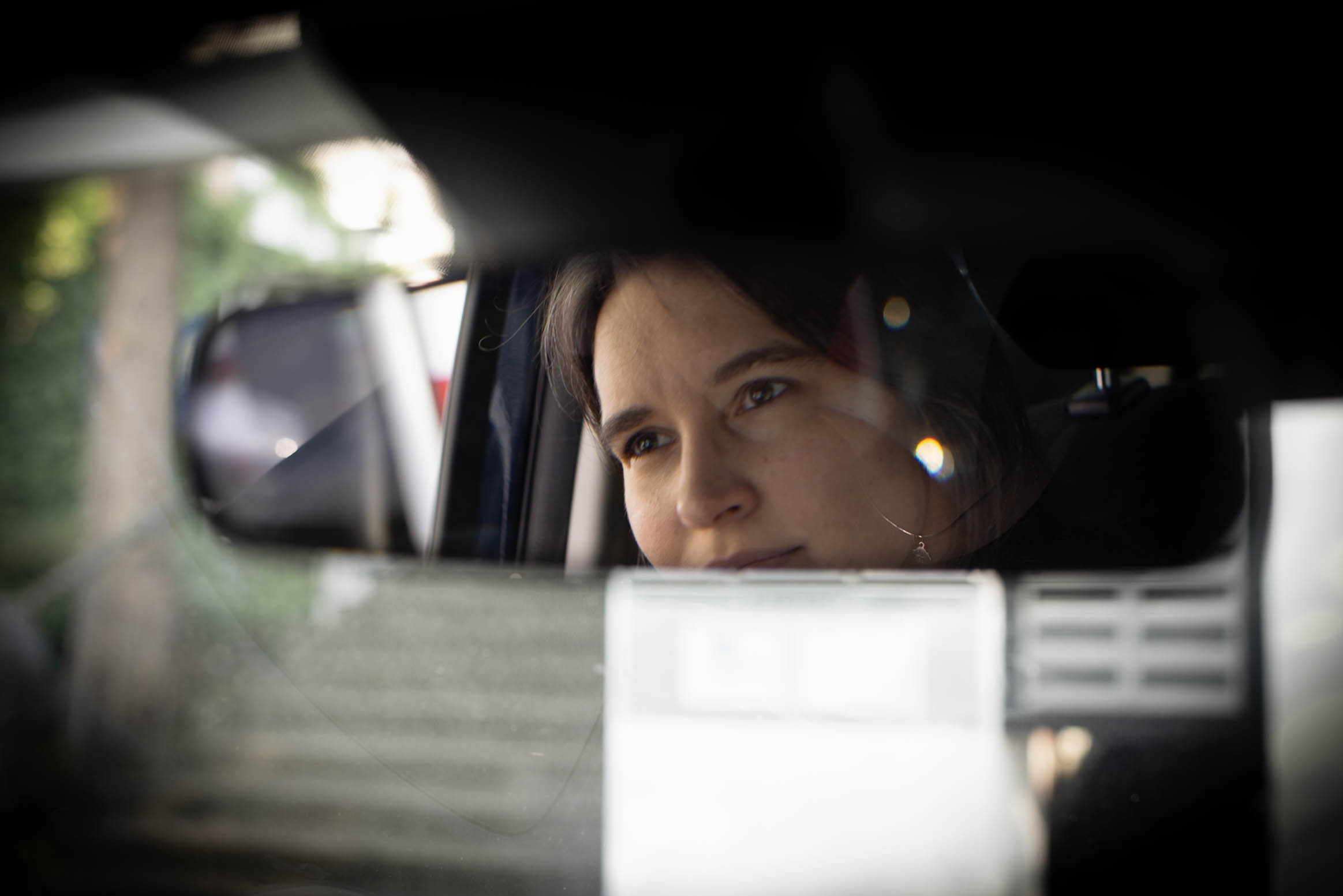 Młoda kobieta o ciemnych oczach odbija się w lusterku samochodowym, patrzy w dal