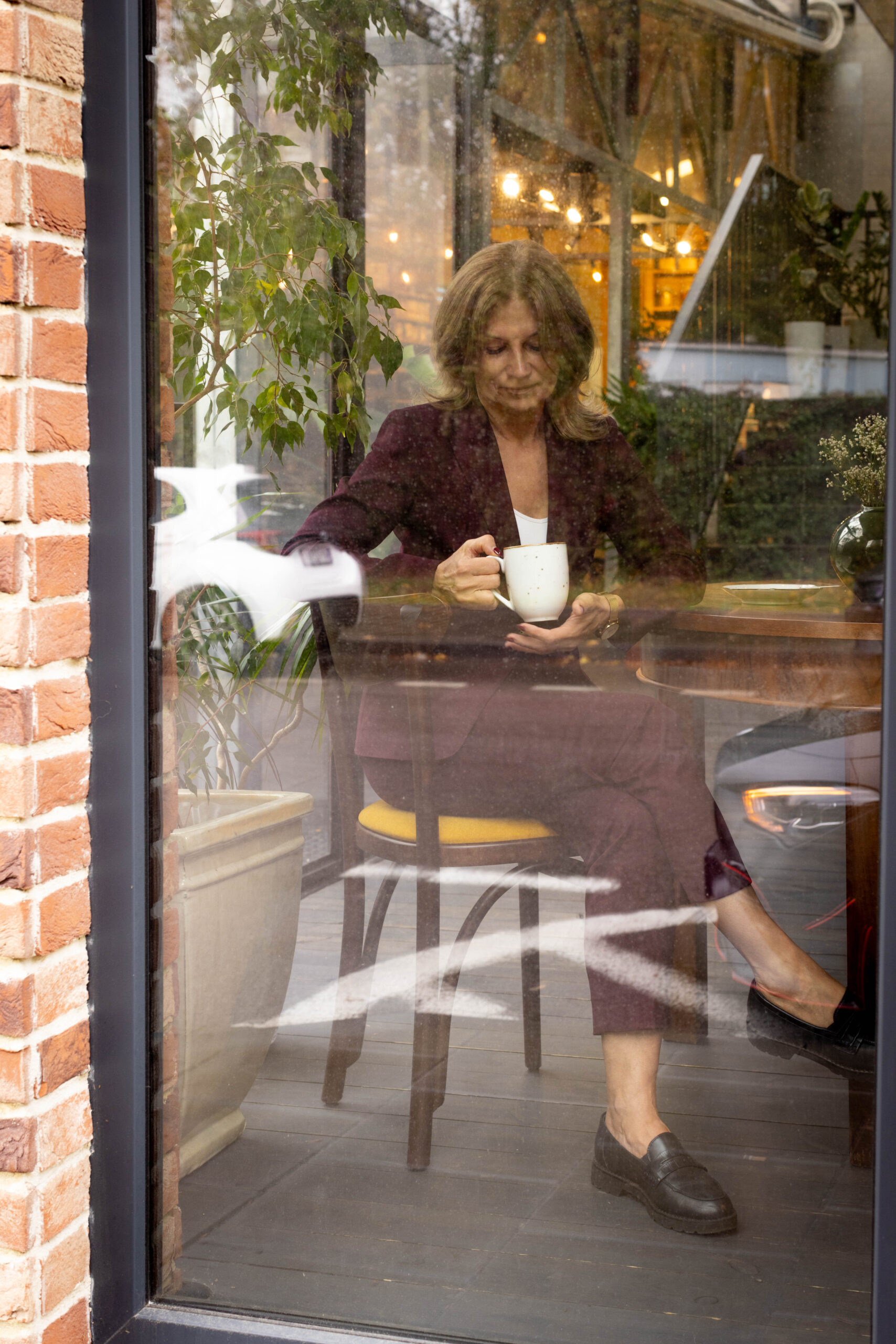 Zdjęcie przez szybę kawiarni kobiety bordowym garniturze trzymającej filiżankę herbaty