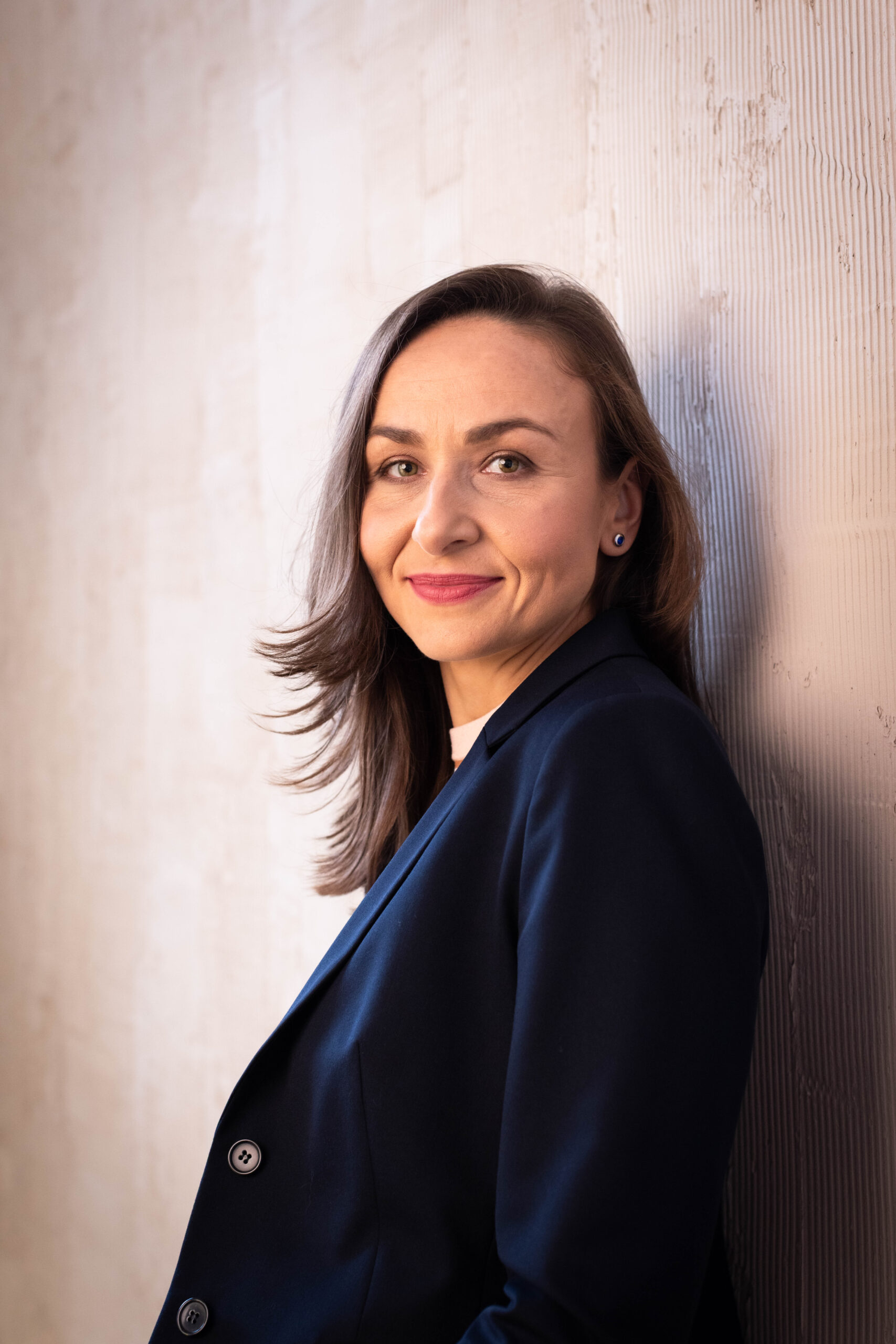 Młoda kobieta o kasztanowych włosach, w granatowej marynarce, pozuje do zdjęcia wizerunkowego w studio