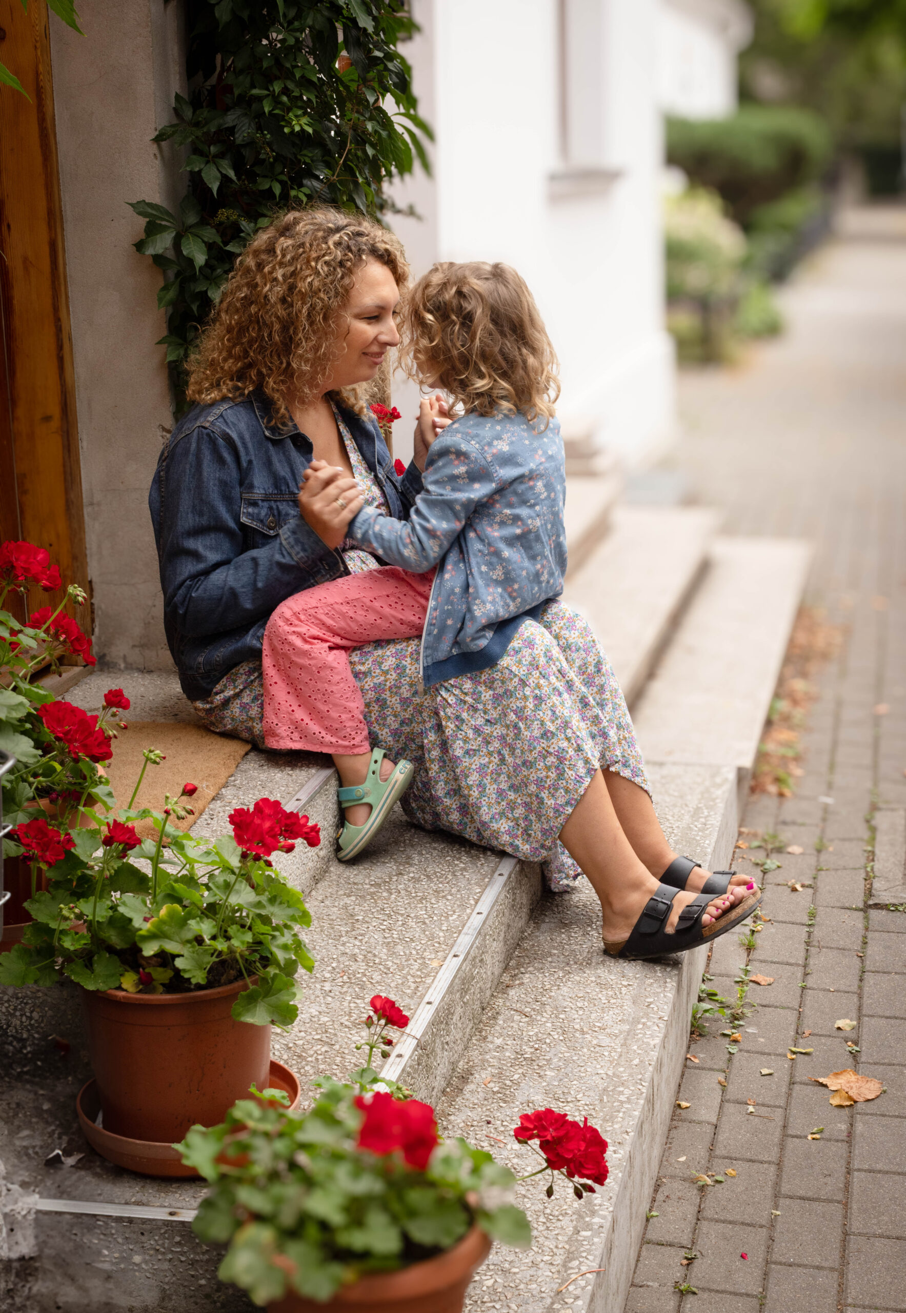 Dziewczynka i mama siedzą na schodach wśród kwiatów i bawią się