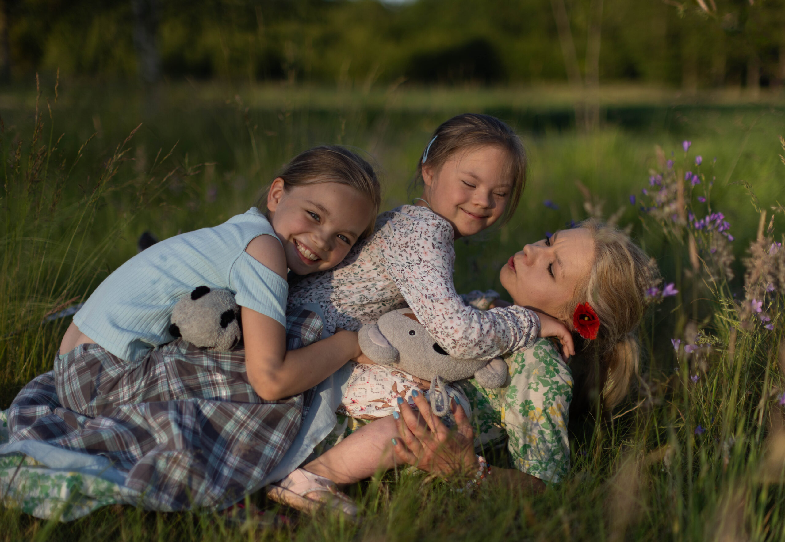 Mama z córkami leżą na trawie wśród kwiatów, przytulone i radosne