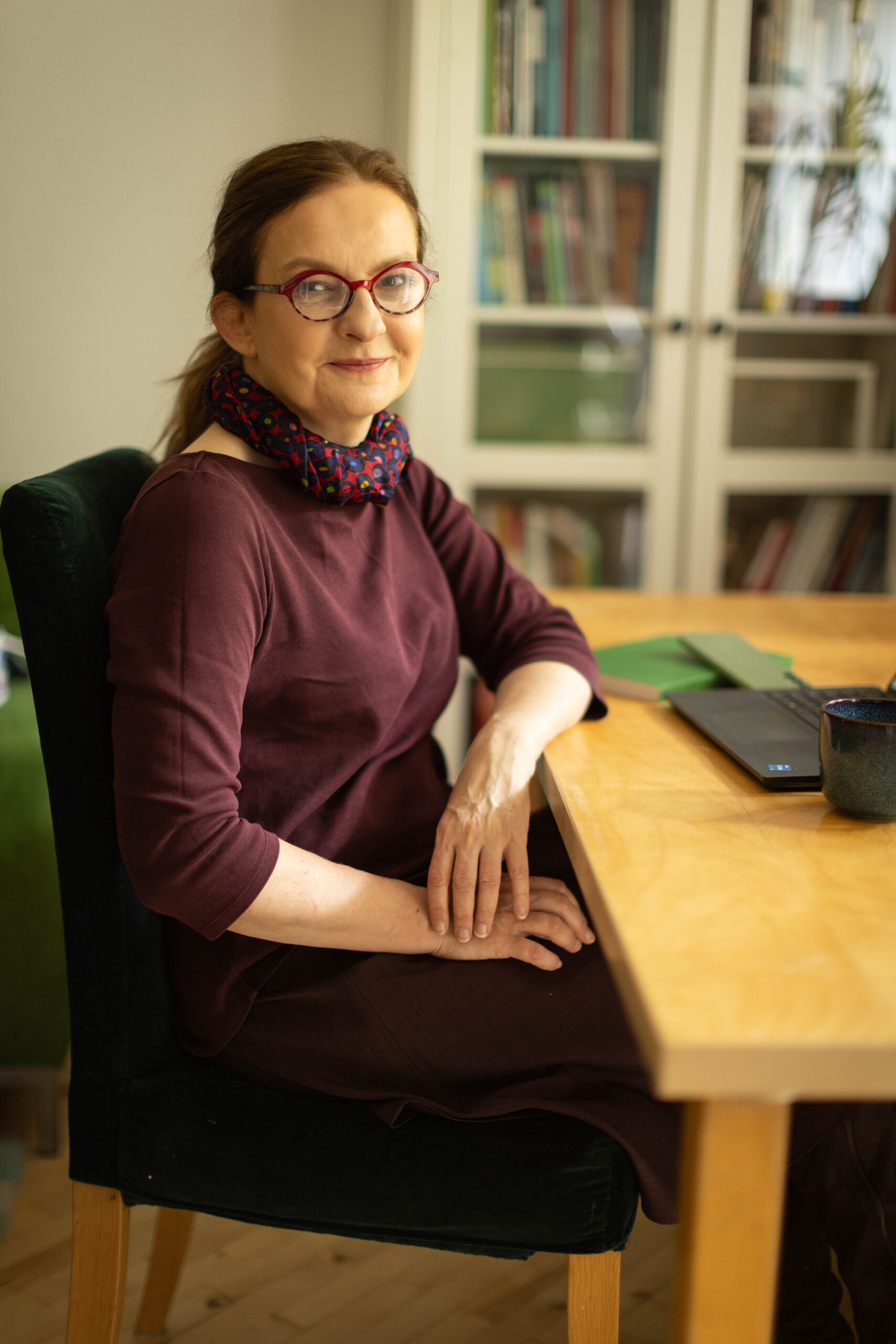 Rudowłosa kobieta w czerwonych okularach siedzi przy biurku