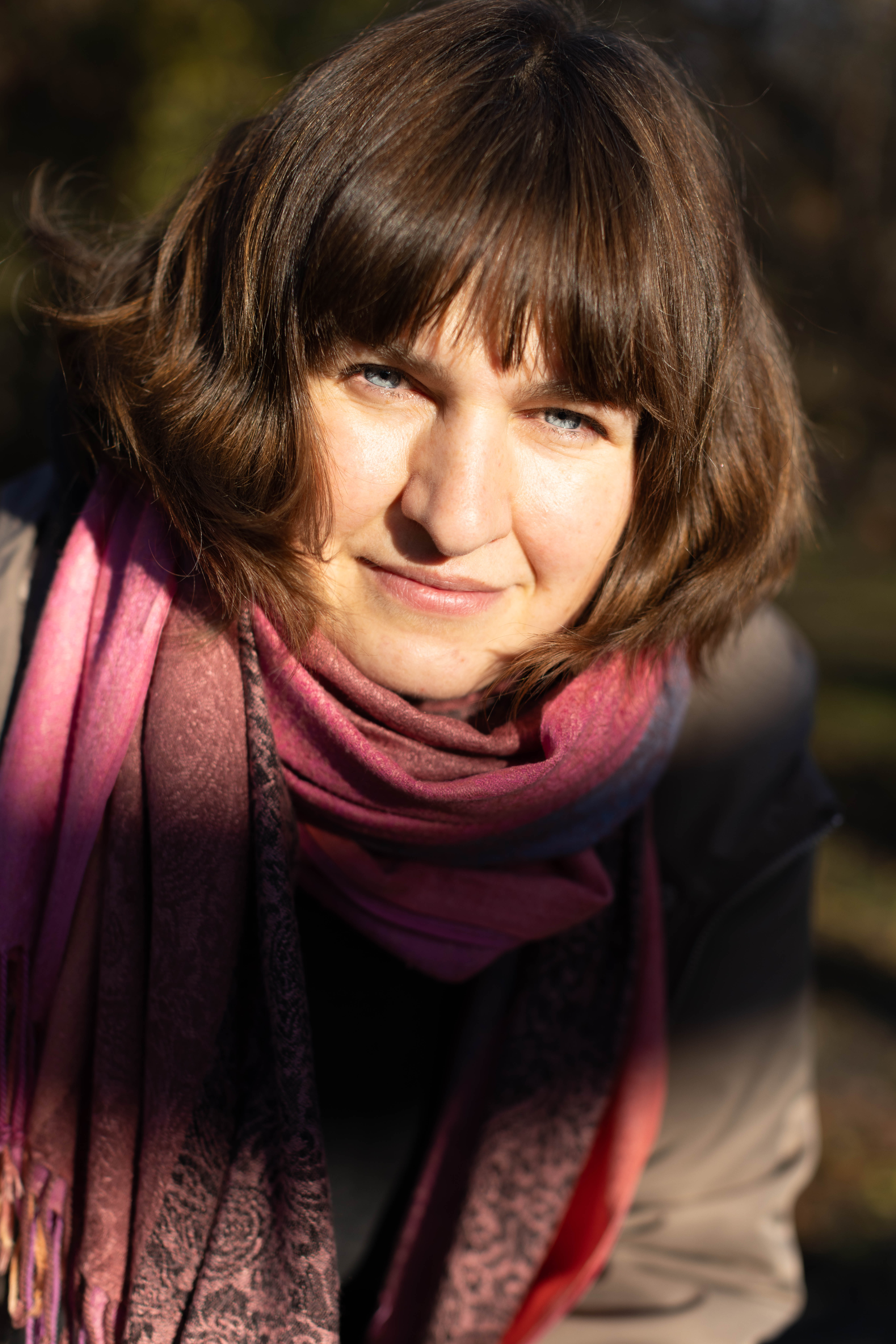 Szatynka uśmiecha się mrużąc oczu w jesiennym słońcu