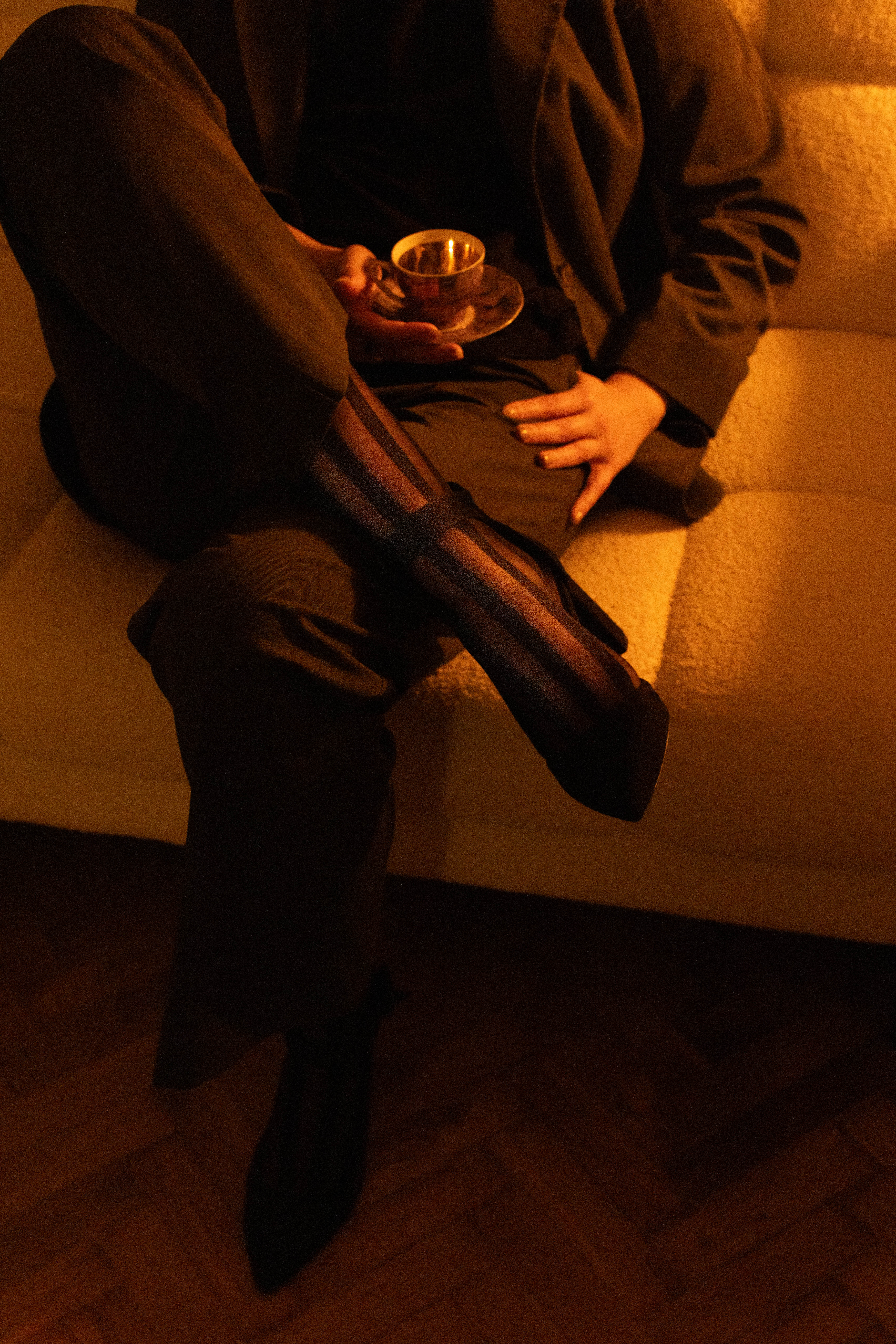 Kobieta we wzorzystych rajstopach i na obcasach siedzi na kanapie z filizanką