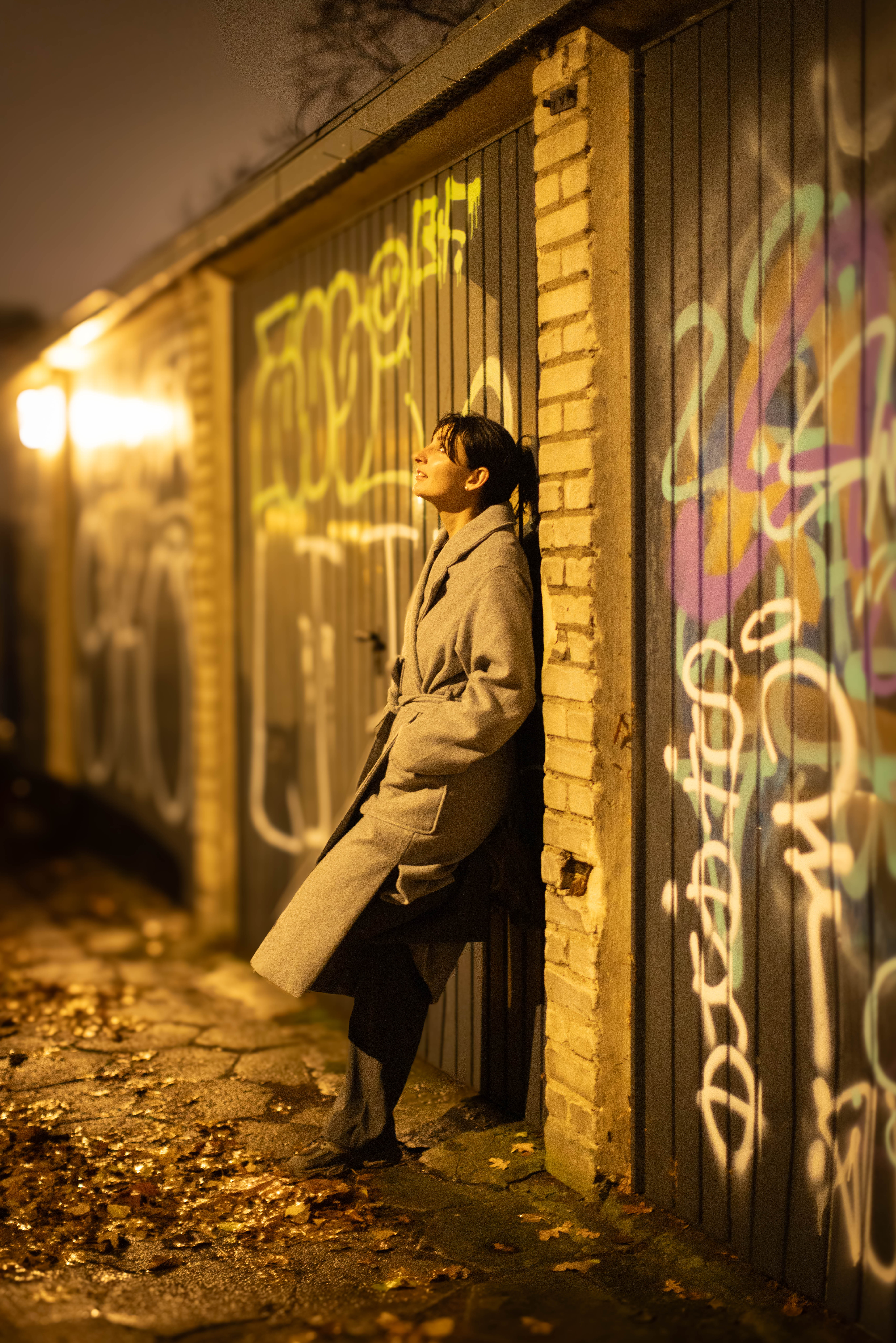 Dziewczyna w płaszczu pozuje nocą na tle garaży