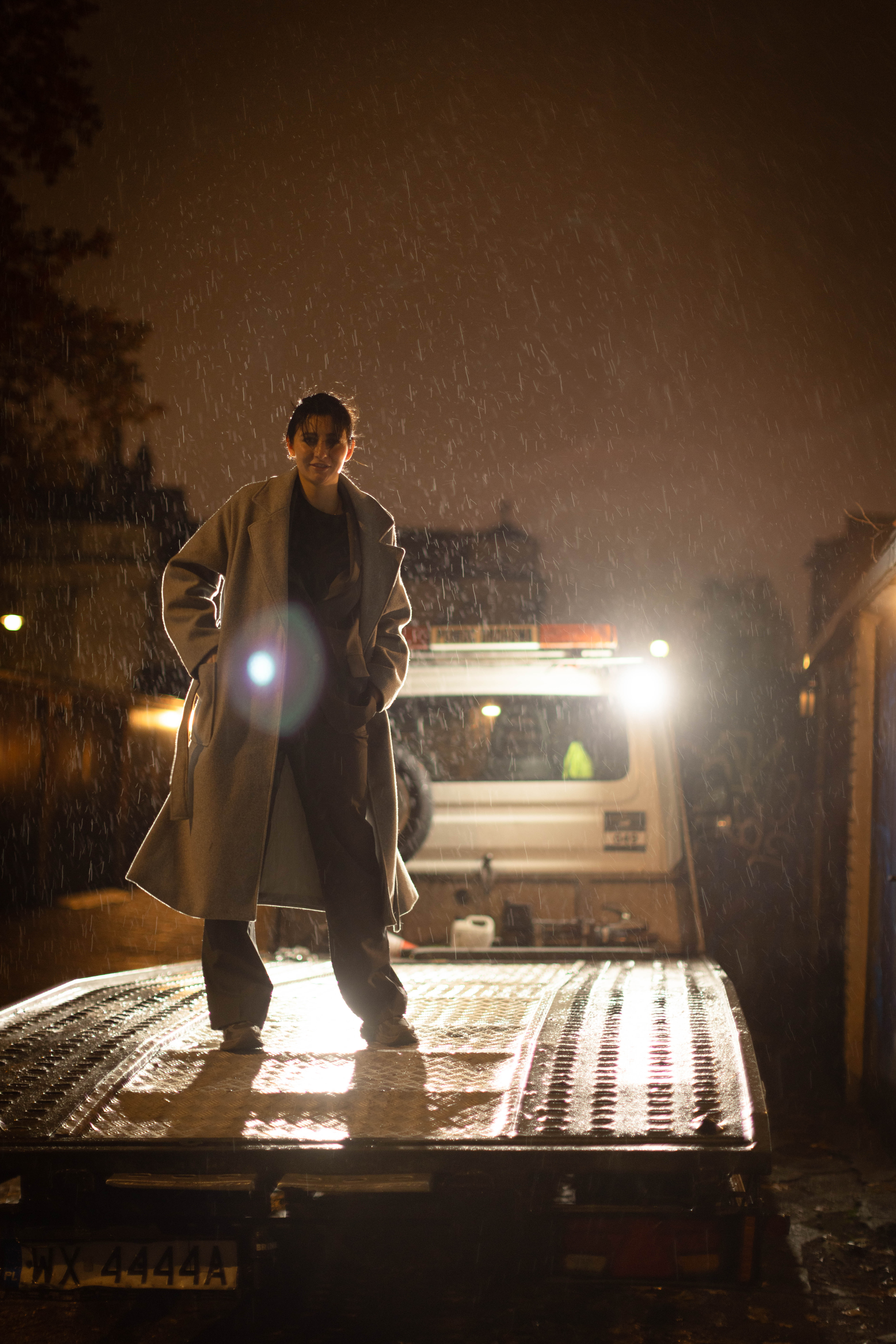 Dziewczyna w płaszczu pozuje nocą w deszczu na lawecie