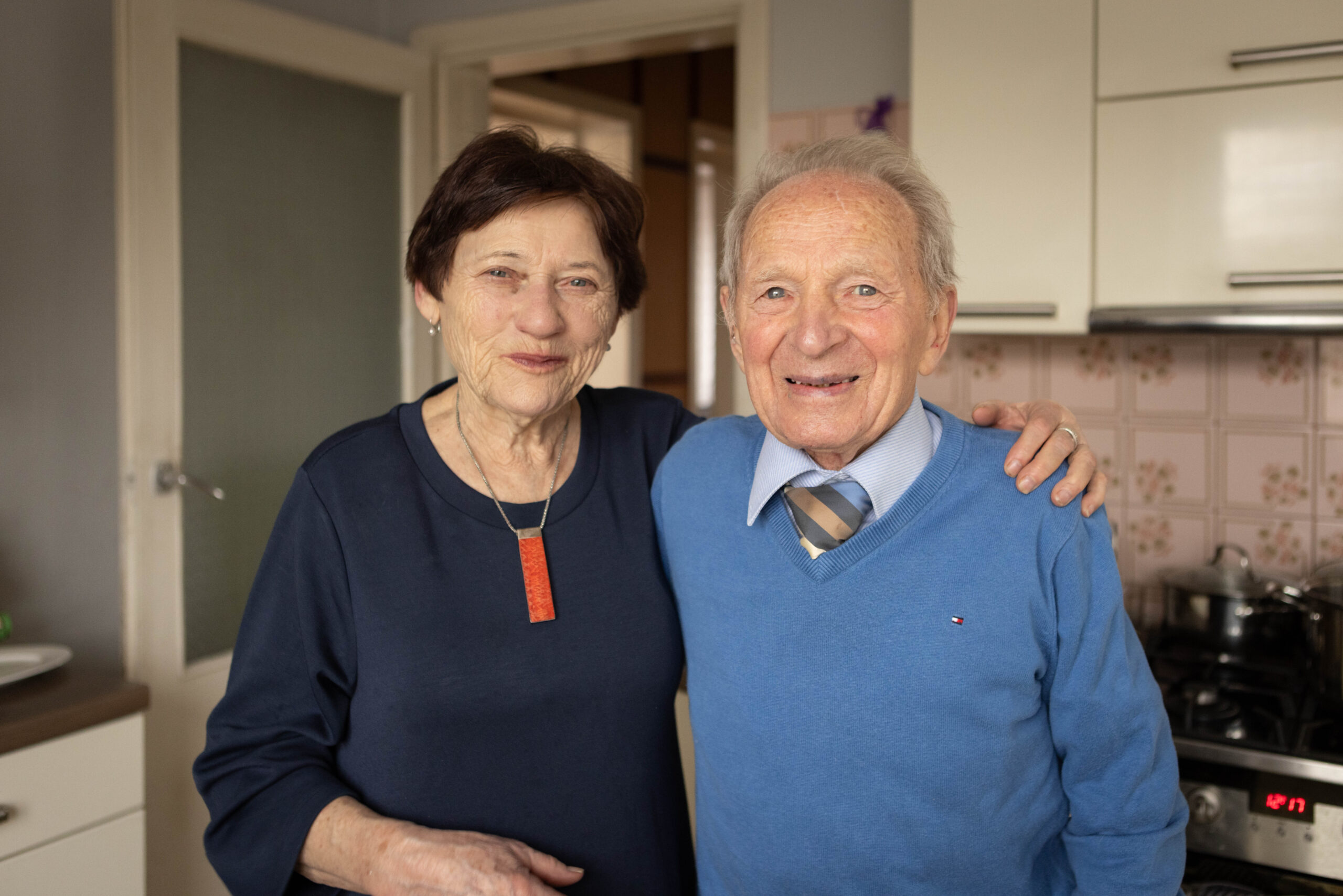 Starsze małżeństwo uśmiechnięte i objęte pozuje do zdjęcia w swojej kuchni, rodzinna sesja zdjęciowa babcia dziadek fotograf Jagoda Rogoża