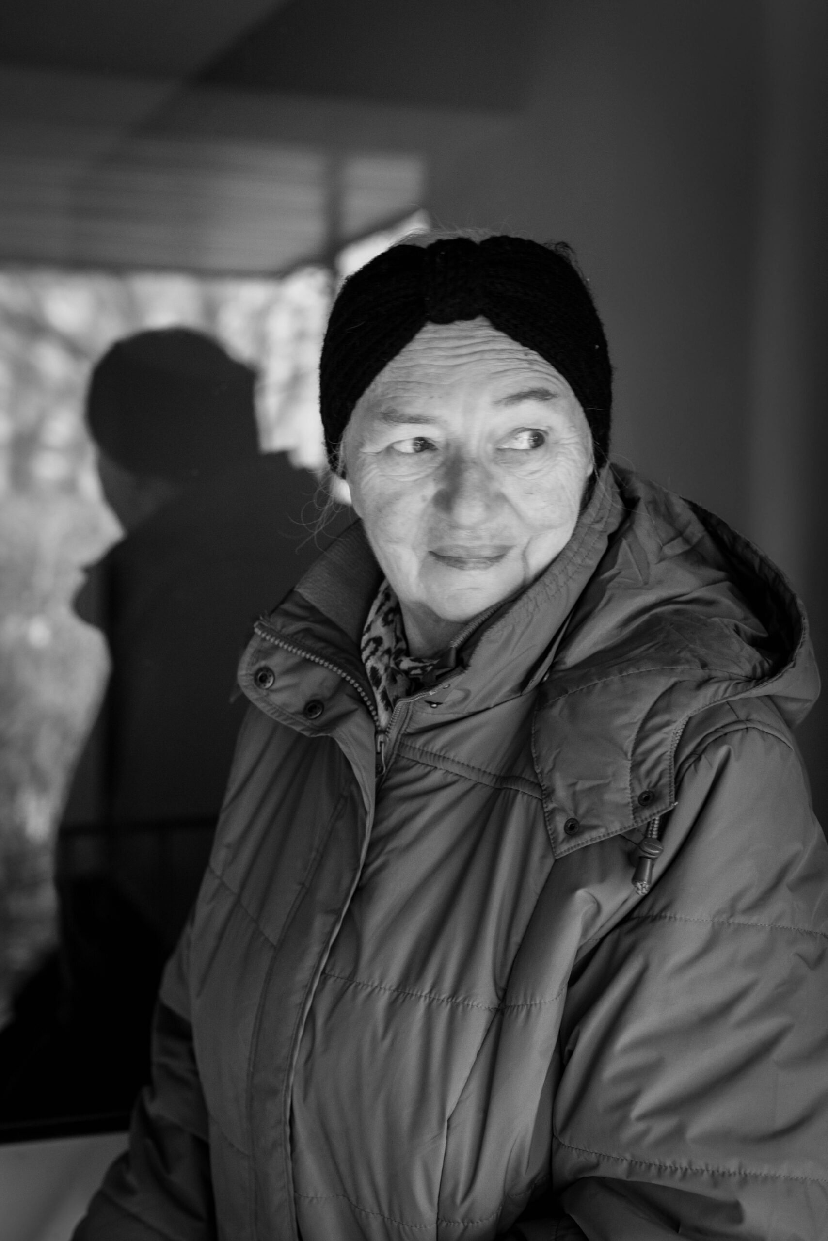 Czarno-białe zdjęcie starszej pani przy klatce schodowej, z odbiciem w szybie