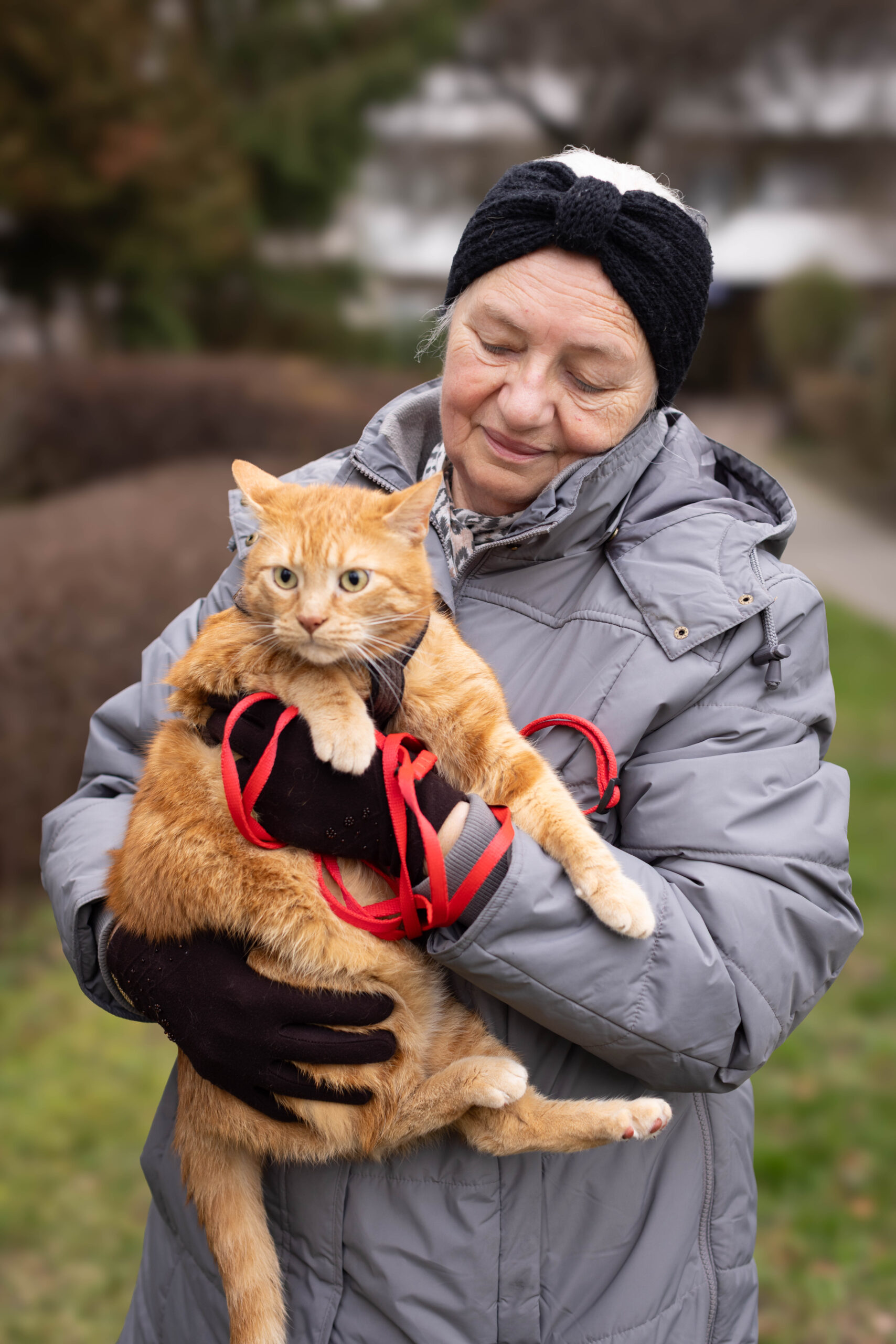 Starsza pani na dworze trzyma na rękach rudego kota, sesja zdjęciowa dla seniorów prezent na dzień babci i dziadka