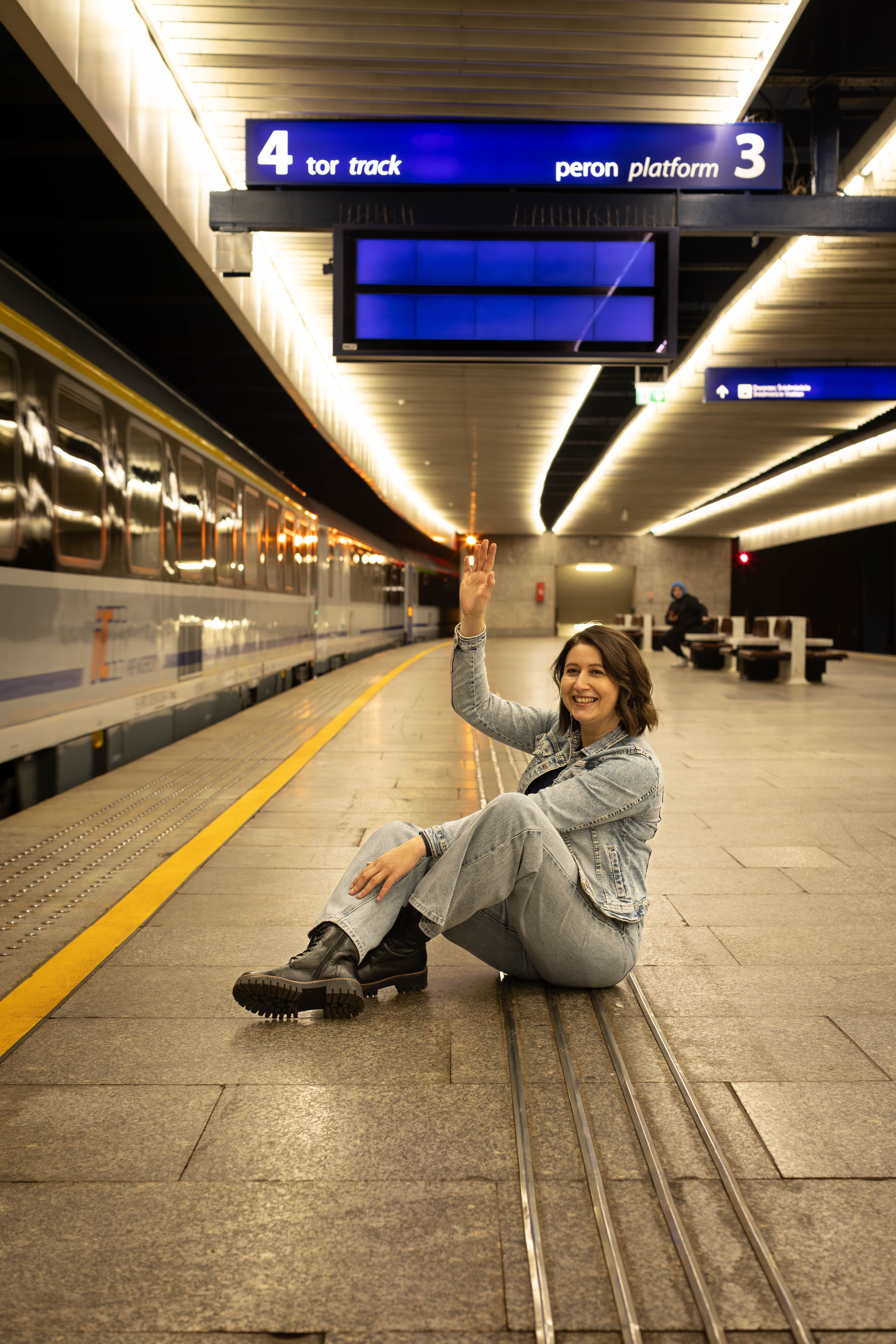 Ciemnowłosa kobieta siedzi na peronie i macha do pociągu