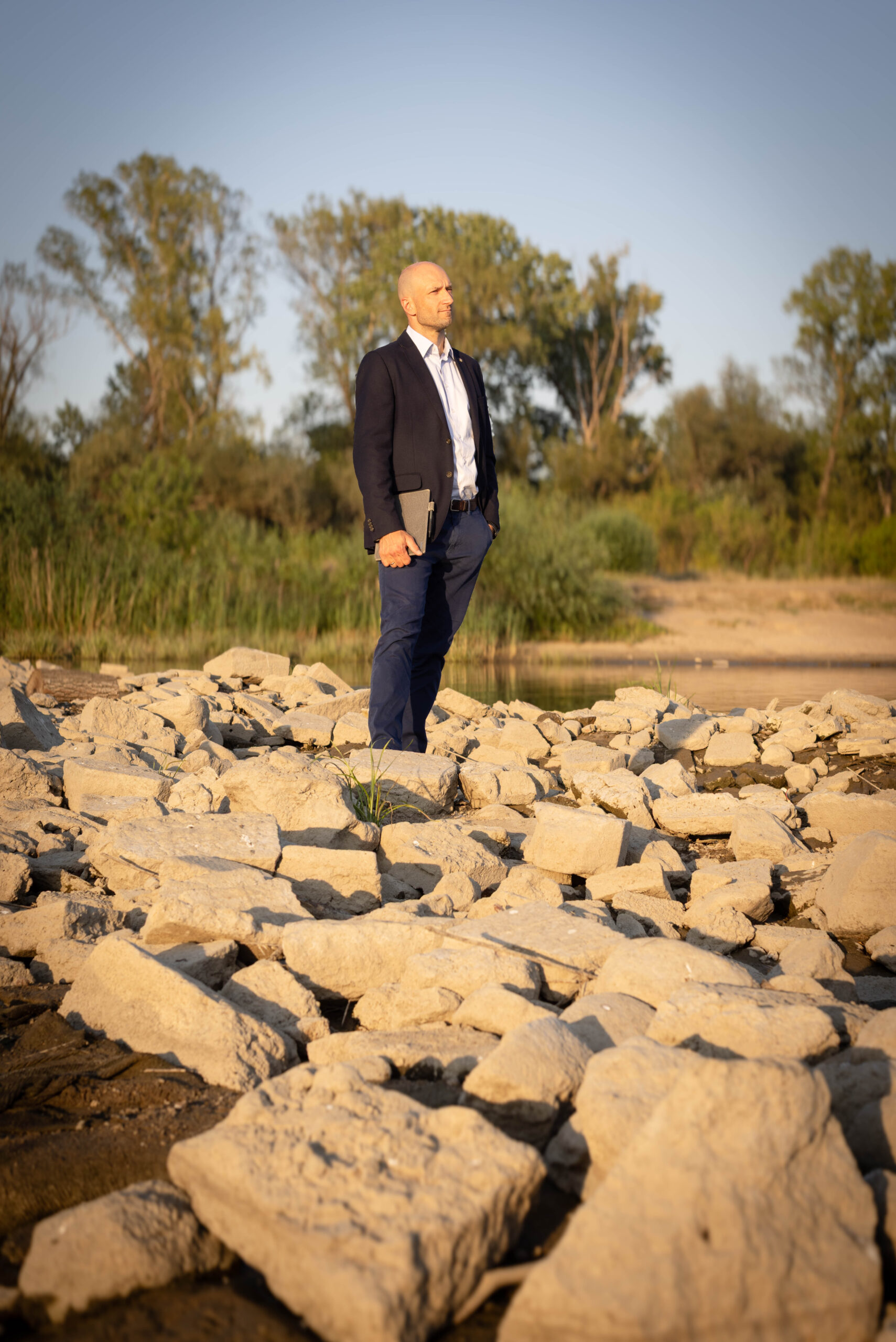 Mężczyzna w marynarce na kamienistym brzegu rzeki