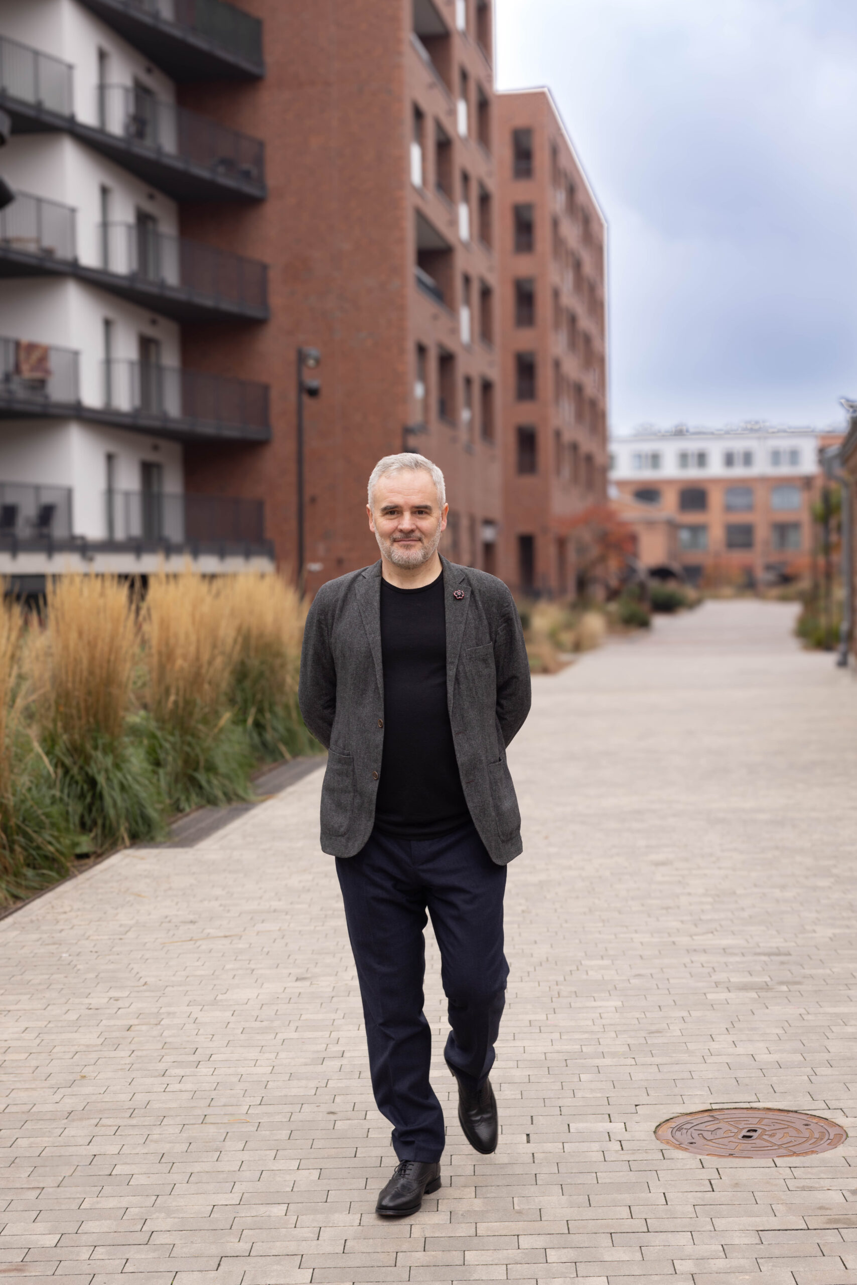 Mężczyzna w szarej marynarce spaceruje po podwórku w przestrzeni loftowej