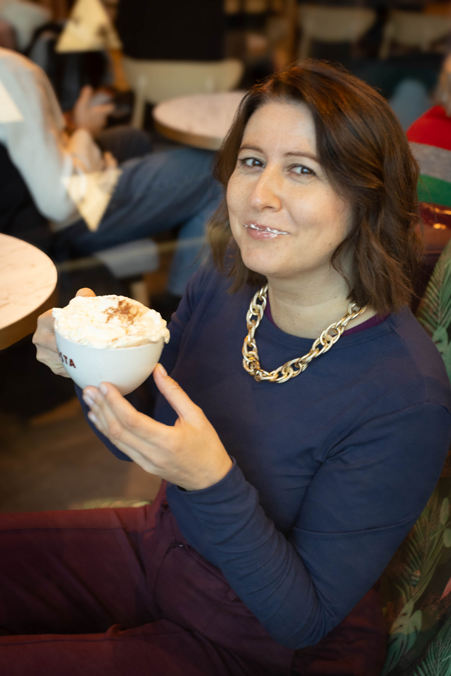 Młoda szatynka w kawiarni pije capuccino z pianką na ustach